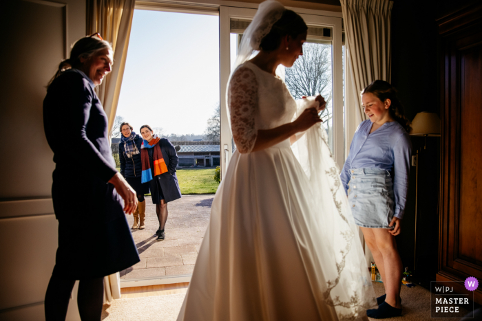 Ein Top-Hochzeitsfotograf in den Niederlanden hat dieses Bild der Braut aufgenommen, die den Gästen ihr Kleid zeigt, während sie auf die Ankunft des Bräutigams wartet