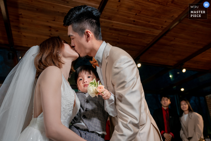 A wedding photographer in Taipei created this image of The couple kissing at the ceremony holding their son