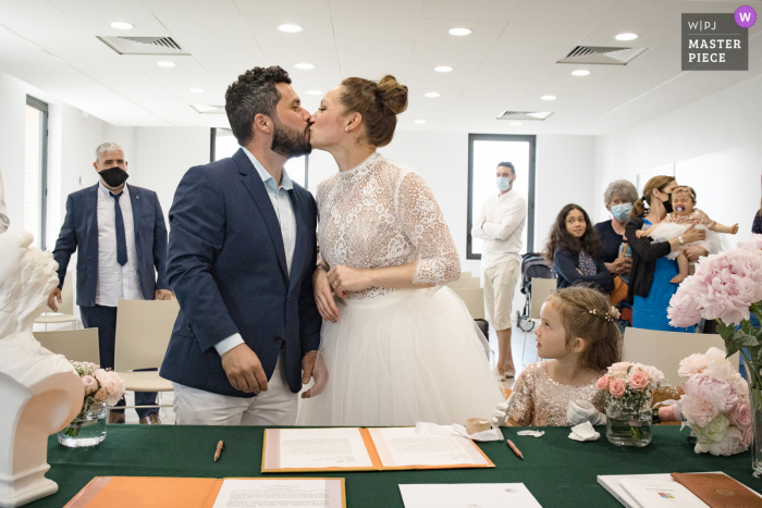 La mejor fotografía de boda del Ayuntamiento de Puyjaudran que muestra una foto que muestra a los novios besándose bajo la atenta mirada de su hija