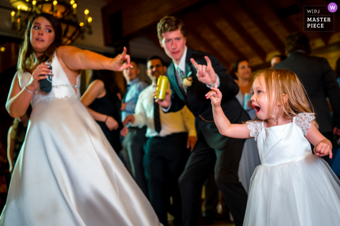 Een top huwelijksfotograaf in Charlottesville, VA bij Mt. Ida Farm maakte deze foto waarop een bloemenmeisje een dansbeweging maakt met de bruid en bruidegom