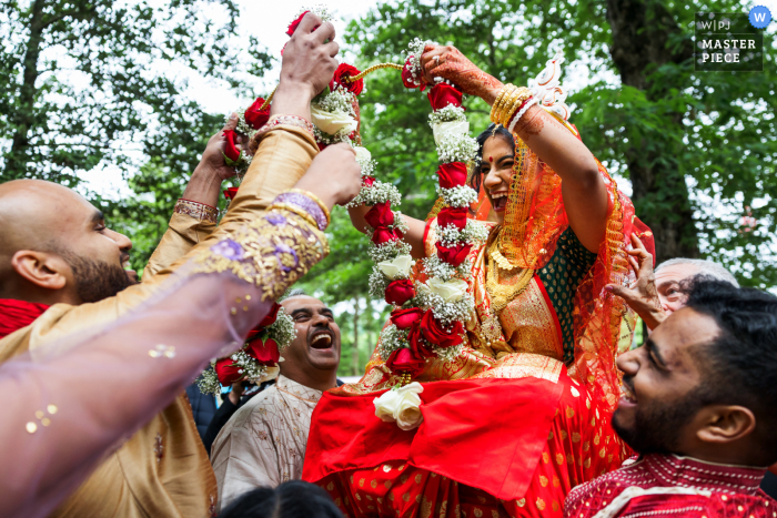 Fotografia di matrimonio dalla storica chiesa Polegreen che mostra la sposa e lo sposo che cercano di ottenere le loro ghirlande di fiori l'una sull'altra durante Biye