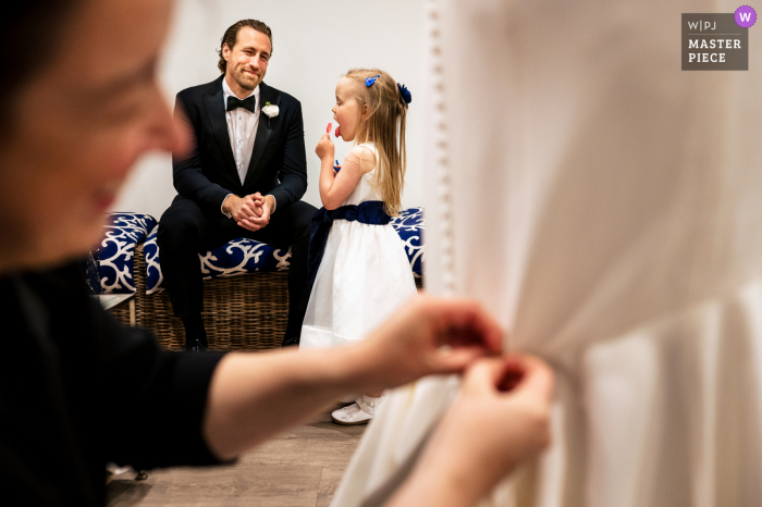 Wychmere Beach Club, Harwich, MA wedding photography of The flower girl eating a lollipop while the bride gets bustled Wychmere Beach Club, Harwich, MA wedding photography of The flower girl eating a lollipop while the bride gets bustled
