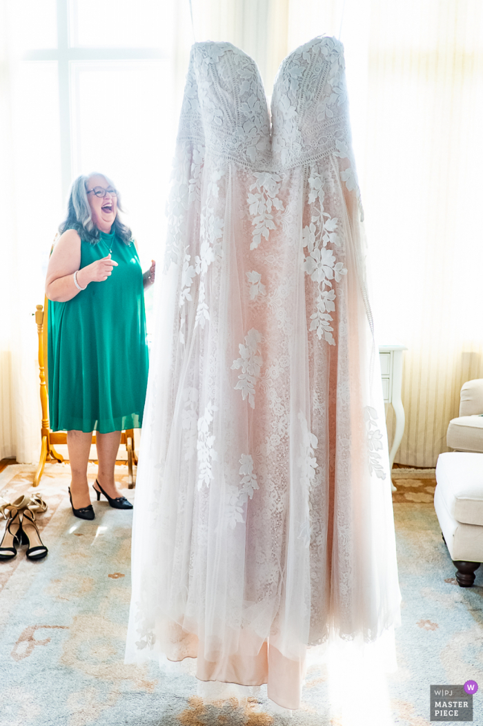 Rhodes Hall, Atlanta nuptial day award-winning image of the mother of the bride laughing as the bride's dress is hanging from the chandelier. The world's best wedding photography competitions are hosted by the WPJA