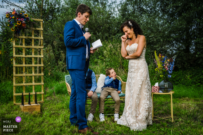 Imagen premiada de la ceremonia de matrimonio al aire libre en Limburgo que muestra a los niños aburridos durante los votos. Los mejores concursos de fotografía de bodas del mundo presentados por la WPJA