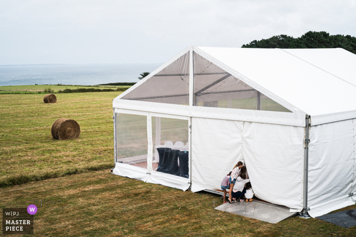 Photo primée de la réception de mariage en plein air de Belle-île qui a enregistré des enfants regardant dans la tente de réception. Les meilleurs photographes de mariage au monde concourent à la WPJA