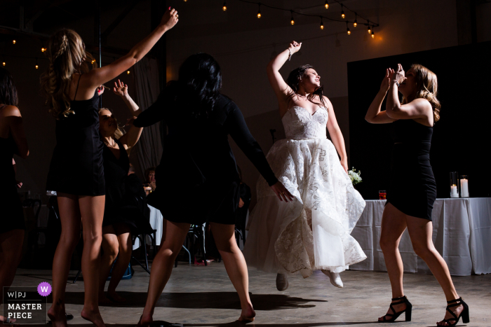 Clay Venues, Colorado Springs indoor wedding reception party award-winning picture showing the bride and her besties jump for joy while celebrating at the reception Clay Venues, Colorado Springs indoor wedding reception party award-winning picture showing the bride and her besties jump for joy while celebrating at the reception. The world's most skilled wedding photographers are members of the WPJA