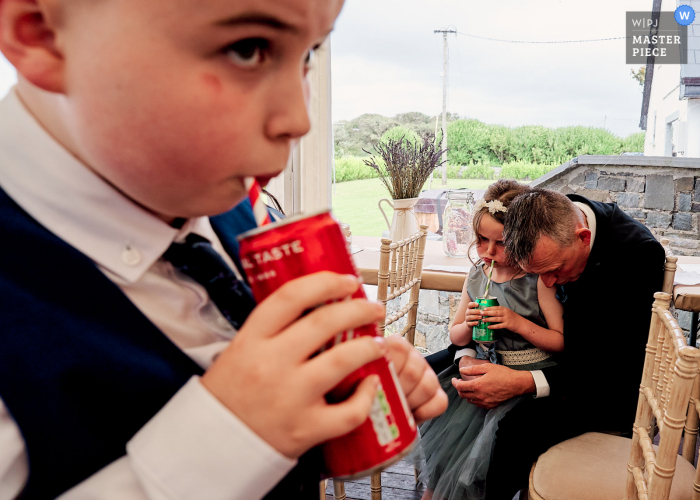 Kilrush, Irland, preisgekröntes Bild zum Hochzeitstag eines Vaters, der verzweifelt den Kopf senkt, während das Geschwister glücklich seine Cola trinkt. Die weltbesten Hochzeitsfotografie-Wettbewerbe werden von der WPJA veranstaltet