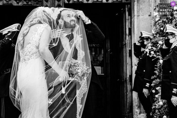 Iglesia de San Ildefonso, Jaén nuptial day award-winning image of groom taking cover under the brides veil with military honors behind