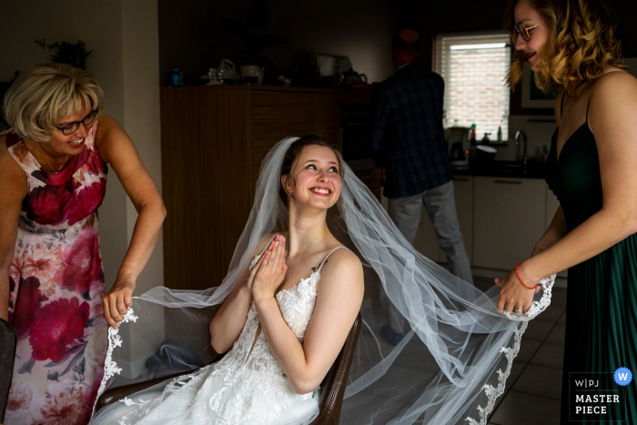 Immagine pluripremiata del momento della preparazione del matrimonio ad Amsterdam che cattura una sposa eccitata in attesa dell'arrivo dello sposo con la sorella e la madre. I migliori concorsi di immagine per matrimoni al mondo sono tenuti dal WPJA