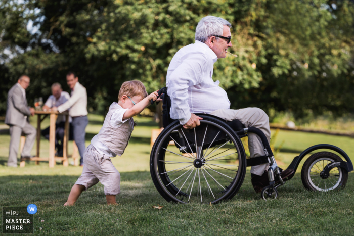 Château Saint Loup en Albret, France réception de mariage en plein air photo primée qui a enregistré un petit garçon poussant un homme en fauteuil roulant sur l'herbe