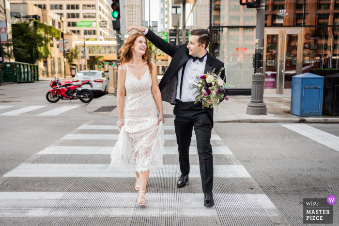 Chicago nuptial day award-winning image of the couple crossing the street while the groom holds the bouquet and fixes the bride's hair. The world's best wedding photography competitions are hosted by the WPJA