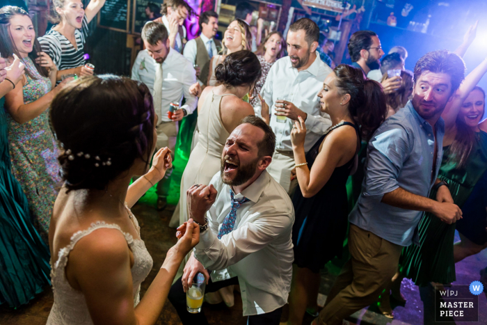 Bonez - Crested Butte, CO Fotografía galardonada de la fiesta de recepción de bodas en interiores que muestra a un novio cantando con todo su corazón en la pista de baile a su esposa. Los fotógrafos de bodas más calificados del mundo son miembros de la WPJA