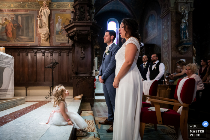 Imagem premiada da cerimônia de casamento na igreja de Sainte Cécile de Fréjairolles mostrando um momento fofo entre a noiva e sua filha na igreja. Os melhores concursos de fotos de casamento do mundo são apresentados através do WPJA