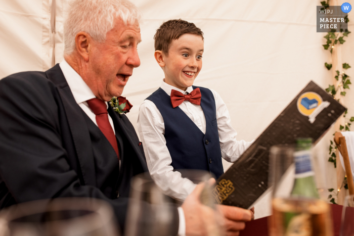 Lake District, United Kingdom indoor wedding reception party award-winning picture with a Page Boy showing Grandad his wedding gift