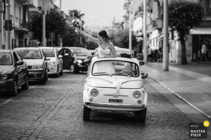 Immagine premiata per il giorno delle nozze del Lazio della sposa che saluta le persone da una piccola auto sulla strada per il ristorante