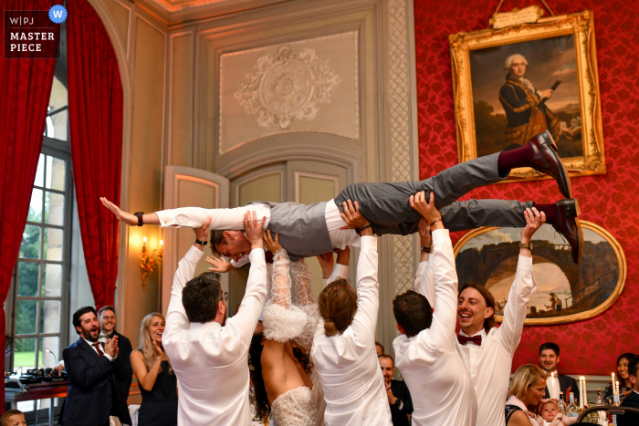 Lille indoor bruiloftsreceptie bekroonde foto met de bruid en bruidsjonkers die de bruidegom vasthouden na hun entreedans