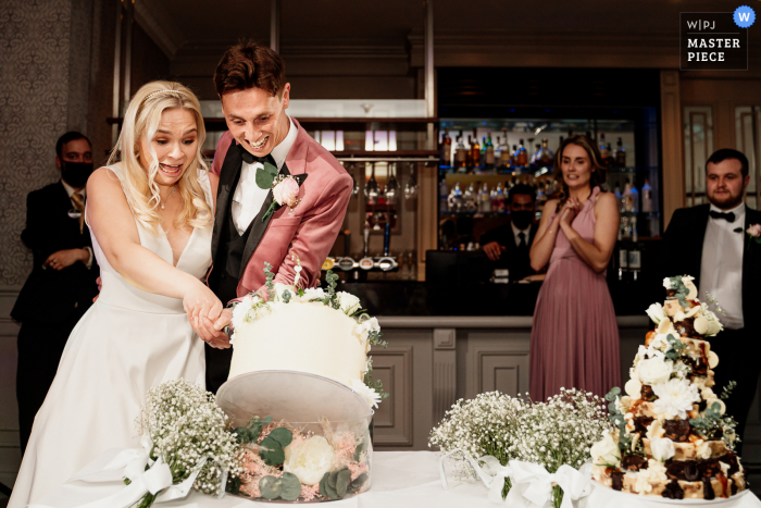 Foto premiada da festa da recepção do casamento no salão Mottram Hall mostrando a noiva e o noivo cortando o bolo e o bolo cai