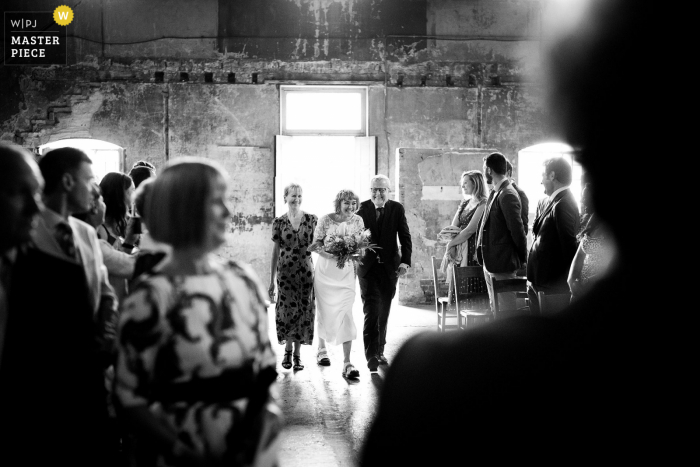 Asylum Chapel, Londres, imagen galardonada de la ceremonia de matrimonio en interiores que muestra a la novia caminando por el pasillo con sus padres y se ríe.