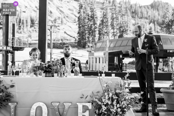 Sugarbowl Resort, Truckee, CA, preisgekröntes Foto der Hochzeitsfeier im Freien, das aufgezeichnet hat Ein Bräutigam reagiert überrascht auf die Rede seines Trauzeugen, während seine Frau lacht