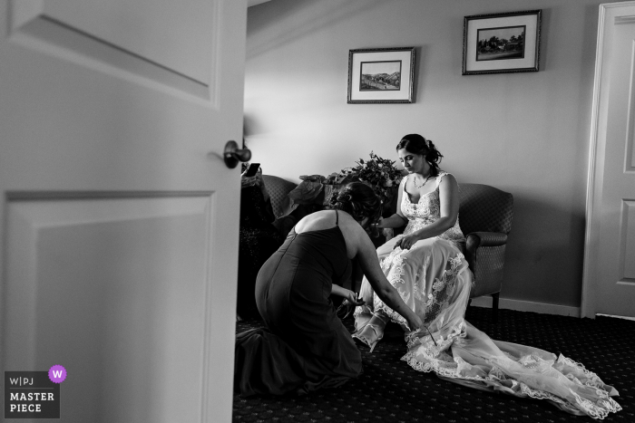 Tempo de preparação do casamento em Bar Harbor, Maine captura de fotos premiadas Uma dama de honra ajuda uma noiva a calçar os sapatos. Os melhores concursos de imagens de casamento do mundo são realizados pela WPJA