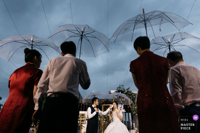 Guangdong Hochzeitstag preisgekröntes Bild einer Hochzeit im Freien im Regen unter Regenschirmen. Die weltbesten Hochzeitsfotografie-Wettbewerbe werden von der WPJA veranstaltet