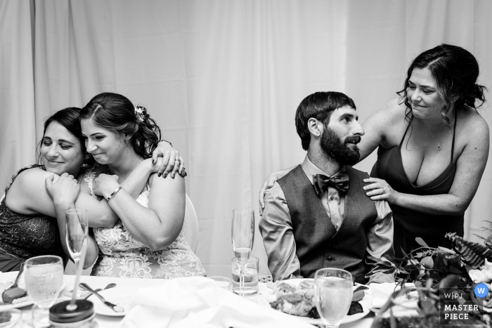 Bar Harbor, Maine indoor wedding reception party award-winning picture showing The bride and groom hug close friends Bar Harbor, Maine indoor wedding reception party award-winning picture showing The bride and groom hug close friends