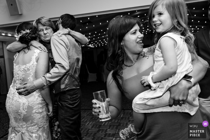 Bar Harbor, Maine indoor wedding reception party award-winning picture showing The bride and groom are hugged while people dance at a wedding reception