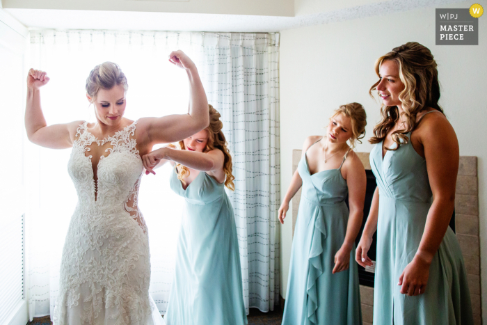 Waterloo Village, Stanhope, New Jersey marriage preparation time award-winning picture capturing the bride flexing as sisters help her into her wedding dress Waterloo Village, Stanhope, New Jersey marriage preparation time award-winning picture capturing the bride flexing as sisters help her into her wedding dress