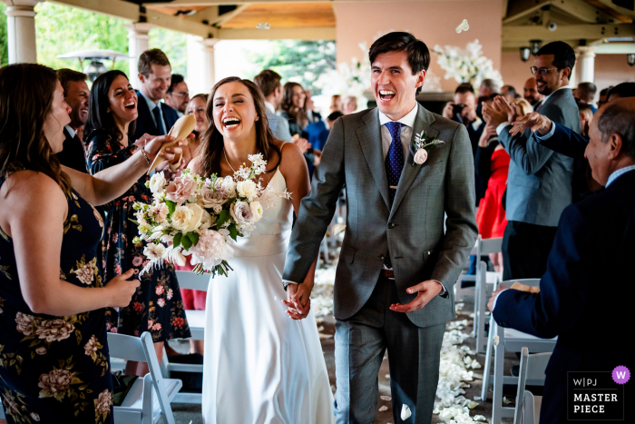 Imagen premiada de la ceremonia de matrimonio en interiores del Hotel Broadmoor, Colorado Springs que muestra a la pareja recibiendo un golpe en la cara con arroz mientras caminan por la isla después de casarse.