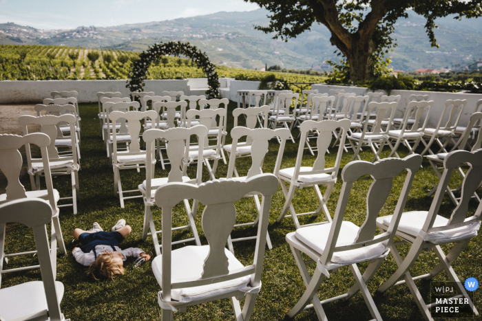 Peso da Régua - Quinta da Pacheca - Portugal Imagen premiada de la ceremonia de matrimonio al aire libre que muestra a un niño pequeño durmiendo junto a las sillas al aire libre. Los mejores concursos de fotografía de bodas del mundo presentados por la WPJA