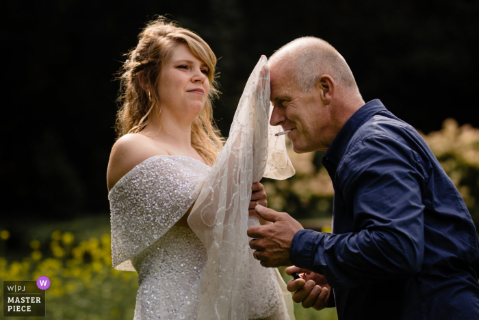 Image primée du jour des noces d'Eeklo de la mariée essuyant la sueur des mariés avec sa robe. Les meilleurs concours de photographie de mariage au monde sont organisés par la WPJA