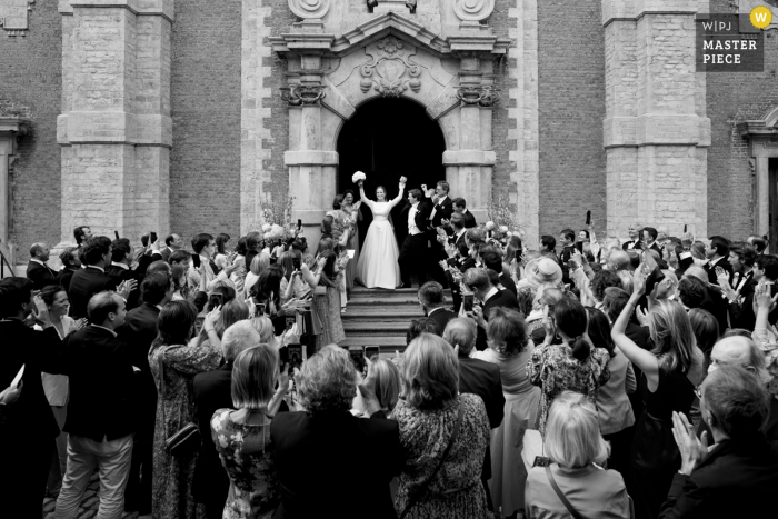 Begijnhof Lier imagen galardonada del día nupcial de la pareja saliendo de la iglesia rodeada de invitados celebrando. Los mejores concursos de fotografía de bodas del mundo son organizados por la WPJA