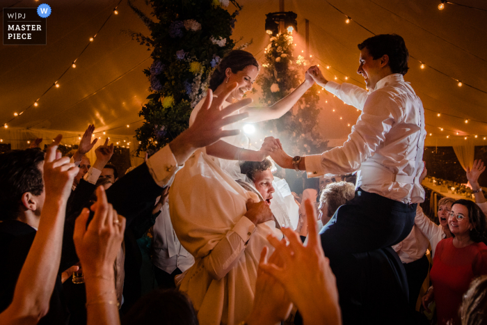 Lier bekroonde foto van een binnenhuwelijksreceptie waarop bruid en bruidegom dansen op de schouders van de gasten. 'S Werelds meest bekwame trouwfotografen zijn lid van de WPJA