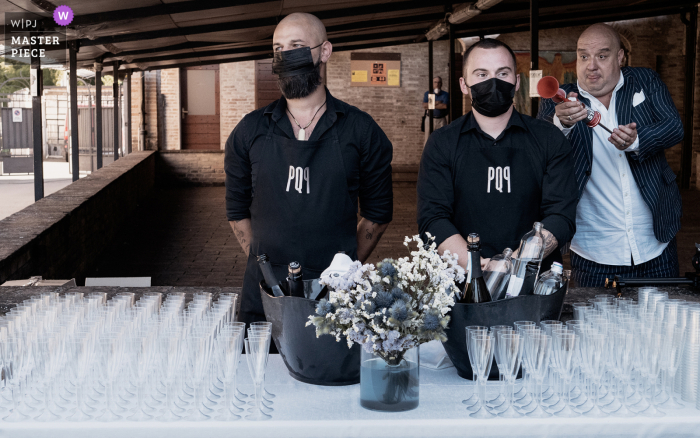 Parma, Italia.Foto ganadora de la ceremonia posterior a la ceremonia de la iglesia al aire libre en el cementerio que alberga la ceremonia de la boda.Se instaló un punto de refrigerio y un invitado está a punto de asustar a los camareros listos para servir vino espumoso a todos.