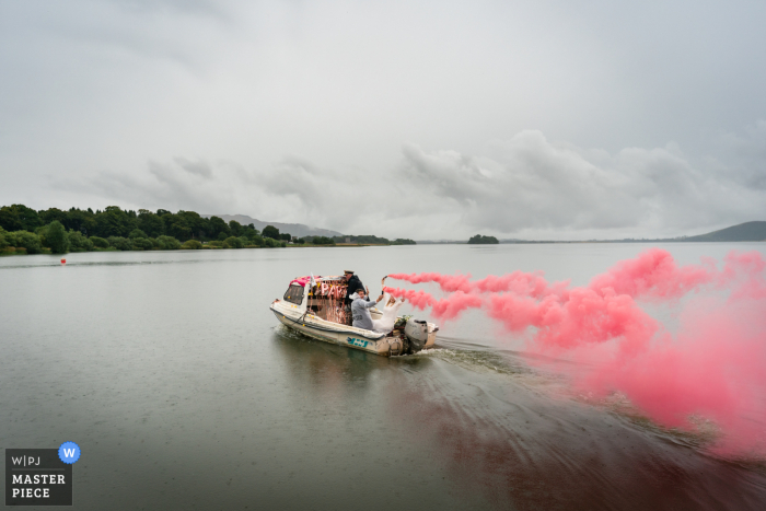 The Boathouse, Kinross outdoor marriage reception party award-winning photo that has recorded the bridal boat streaming smoke bombs. The world's top wedding photographers compete at the WPJA