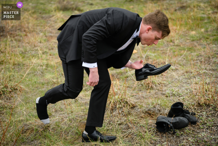 Estes Park, Colorado nuptial day award-winning image of Groom blowing on his shoe to clean it after changing out of his motorcycle boots