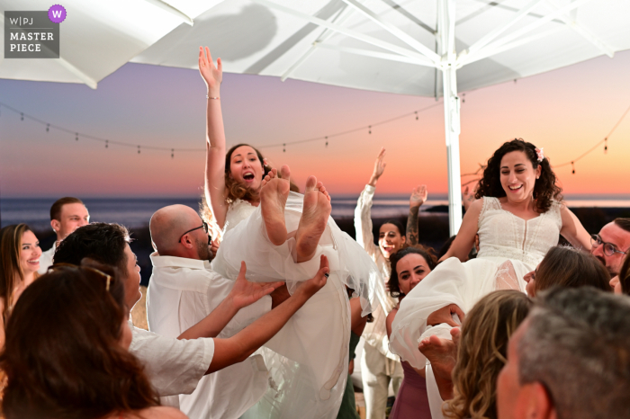 Leblon São João, Costa da Caparica, Lissabon preisgekröntes Foto der Hochzeitsempfangsparty im Freien, das aufgezeichnet hat, wie Gäste das Paar in die Luft werfen. Die besten Hochzeitsfotografen der Welt messen sich bei der WPJA