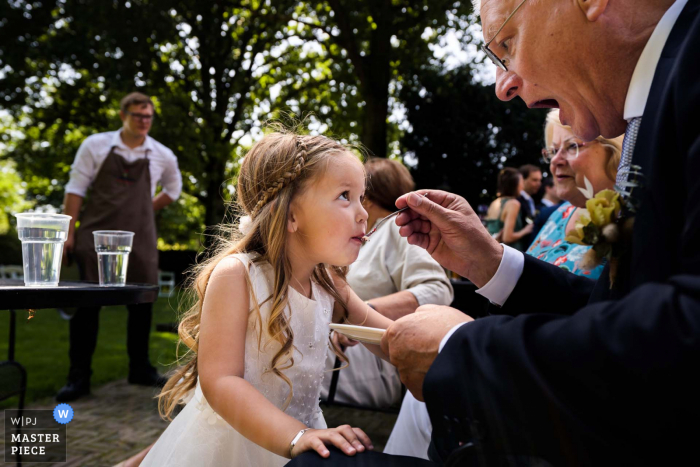 De Landgoederij in Bunnik openlucht huwelijksreceptie bekroonde foto waarop het bloemenmeisje is vastgelegd die taart krijgt van haar opa. 'S Werelds beste trouwfotografen strijden tegen de WPJA