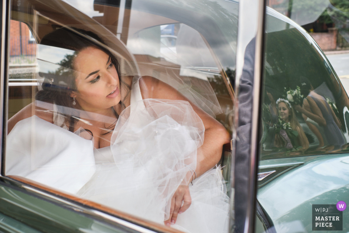 Katholische Kirche St. Marys, Loughborough Hochzeitstag preisgekröntes Bild der Braut beim Aussteigen aus dem Auto, während eines der Blumenmädchen Uhren, spiegelt sich im Heck des Autos