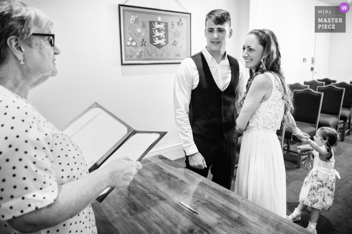 The Greffe, Guernsey marriage ceremony award-winning image showing the Couples daughter wanting attention during the indoor event - from the world's best wedding photography competitions presented by the WPJA