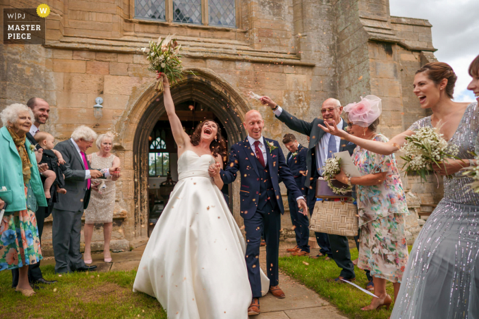 Imagen premiada de la ceremonia de matrimonio de East Midlands que muestra a la pareja feliz saliendo de la iglesia, de los mejores concursos de fotografía de bodas del mundo presentados por la WPJA