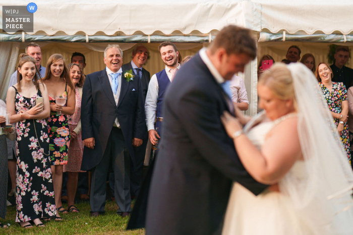 Preisgekröntes Foto der Lincolnshire-Hochzeitsempfangsparty, das den Vater der Braut und die Gäste zeigt, die auf den ersten Tanz von Braut und Bräutigam blicken - aus den weltweit besten Hochzeitsfotografie-Wettbewerben, die von der WPJA angeboten werden