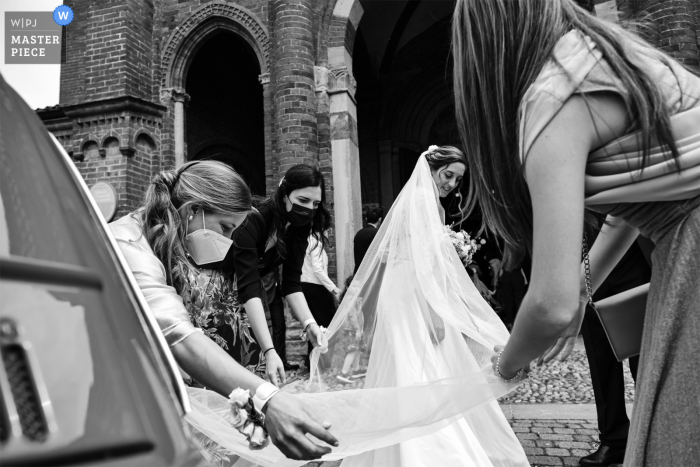 Chiaravalle della Colomba, imagem premiada da cerimônia de casamento de Castell 'Arquato mostrando O arranjo do véu da noiva antes de entrar na igreja - nos melhores concursos de fotografia de casamento do mundo apresentados pela WPJA