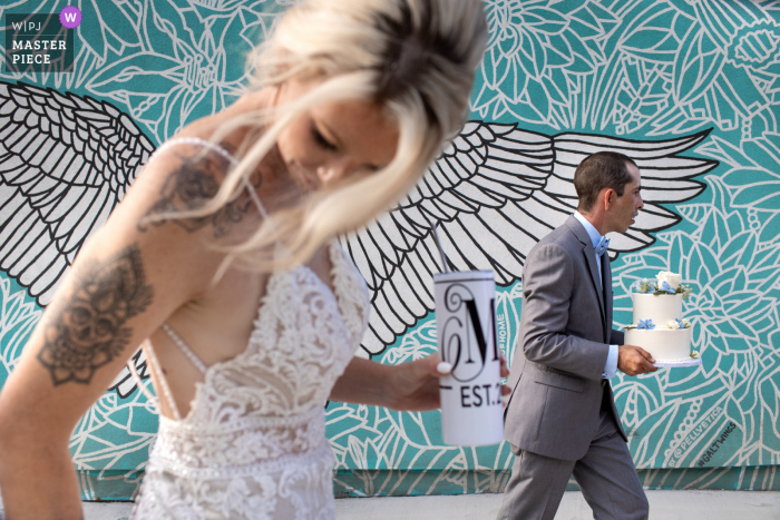 Foto premiada da festa de recepção de casamento em Ontário, Canadá, que gravou Noivo carrega o bolo enquanto a noiva arruma seu vestido - nos melhores concursos de fotografia de casamento do mundo oferecidos pela WPJA