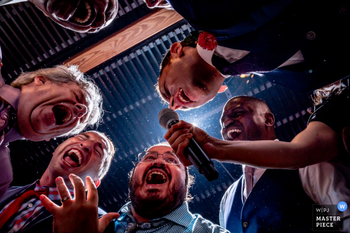 Foto premiada da festa de recepção de casamento em District Winery, Washington DC Um grupo de convidados cantando com o noivo - nos melhores concursos de fotografia de casamento do mundo oferecidos pela WPJA