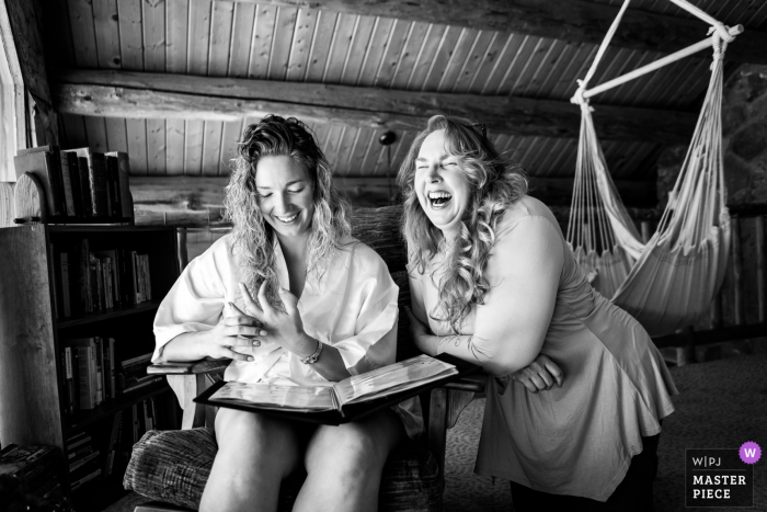 Imagen premiada del día nupcial de Pagosa Springs, Colorado de la novia compartiendo un momento con su madre mientras mira un álbum especial por la mañana, de los mejores concursos de fotografía de bodas del mundo organizados por la WPJA.