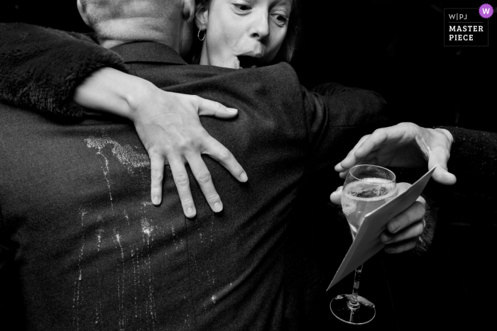 A Hoeve Engelendael documentary-style wedding image showing a moment when a woman spills her drink on the back of a mans suit during a hug