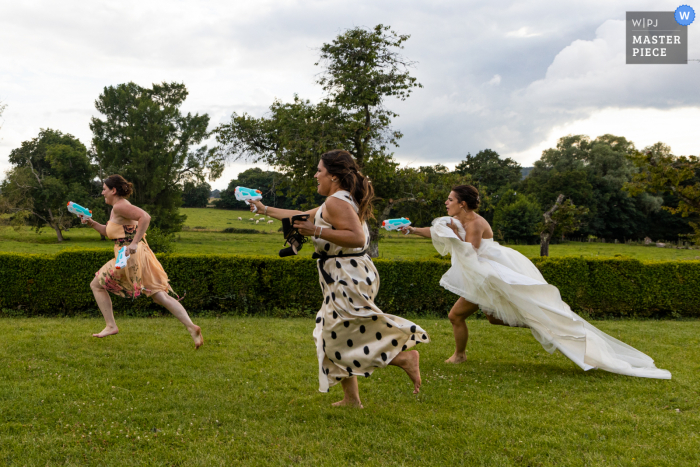 Imagen de una boda de estilo documental en Francia que muestra un momento en el Chateau de Beaujeu de una pelea de agua al aire libre con pistolas