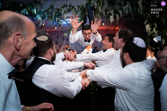 A Hertforshire wedding reportage photographer captured this moment at The Grove of The Groom being thrown through the air