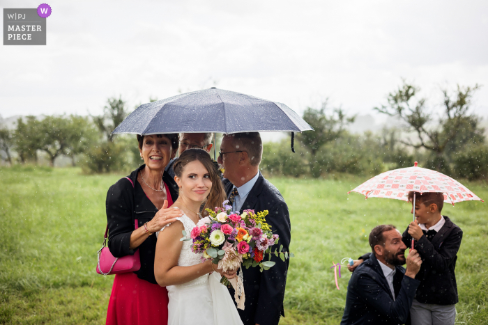 Um fotógrafo de documentários de casamento na França criou esta imagem Poucos minutos antes da cerimônia começar, com um lindo sol, infelizmente, no espaço de um instante começou a chover, aqui a noiva com seus pais, enquanto esperava pela chuva